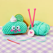 Key lime pie knit kit with green yarn ball, pink needles, and taco plushie