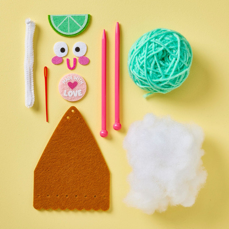 Key lime pie knitting kit with yarn, felt pieces, needles and decorative elements on yellow background