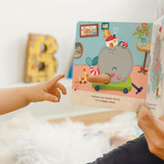 Child's hand pointing at a children's book with a whale illustration on a light-colored surface.