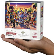 A hand holding a boxed jigsaw puzzle. The front of the box shows an illustrated scene with several people and elephants in a market setting, and the text reads "BOARDWALK: Three Wise Men" and "Personal Puzzle.