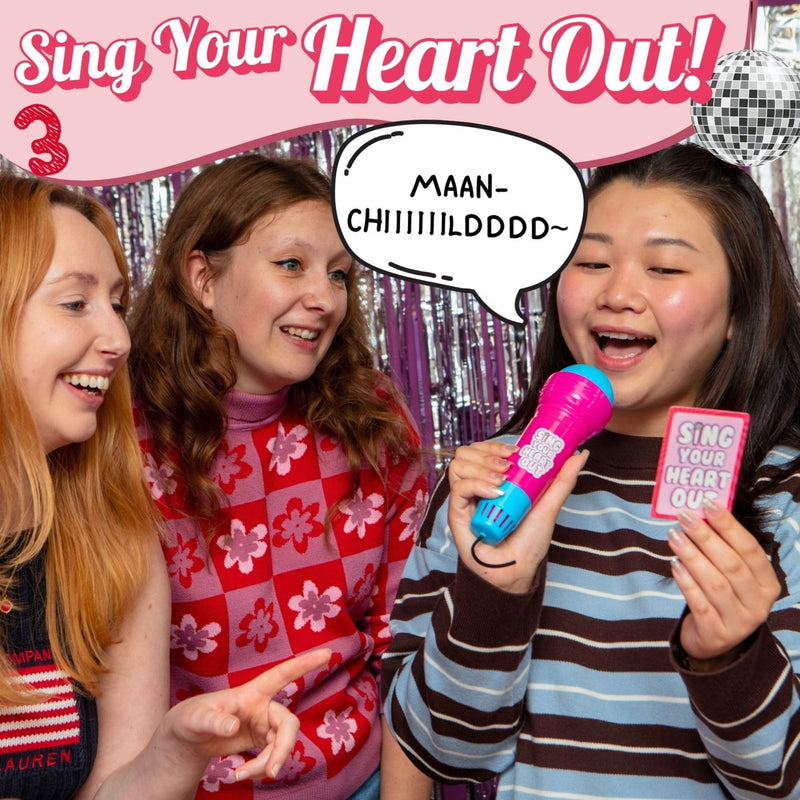 Three friends singing with a microphone and 'Sing Your Heart Out!' sign in a festive setting.