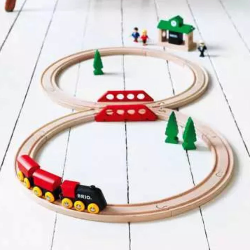 Classic figure 8 wooden train set with a red engine and track on a white wooden surface.