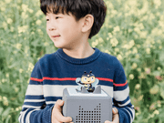 Child holding Toniebox with bee-themed Tonie figure in garden setting