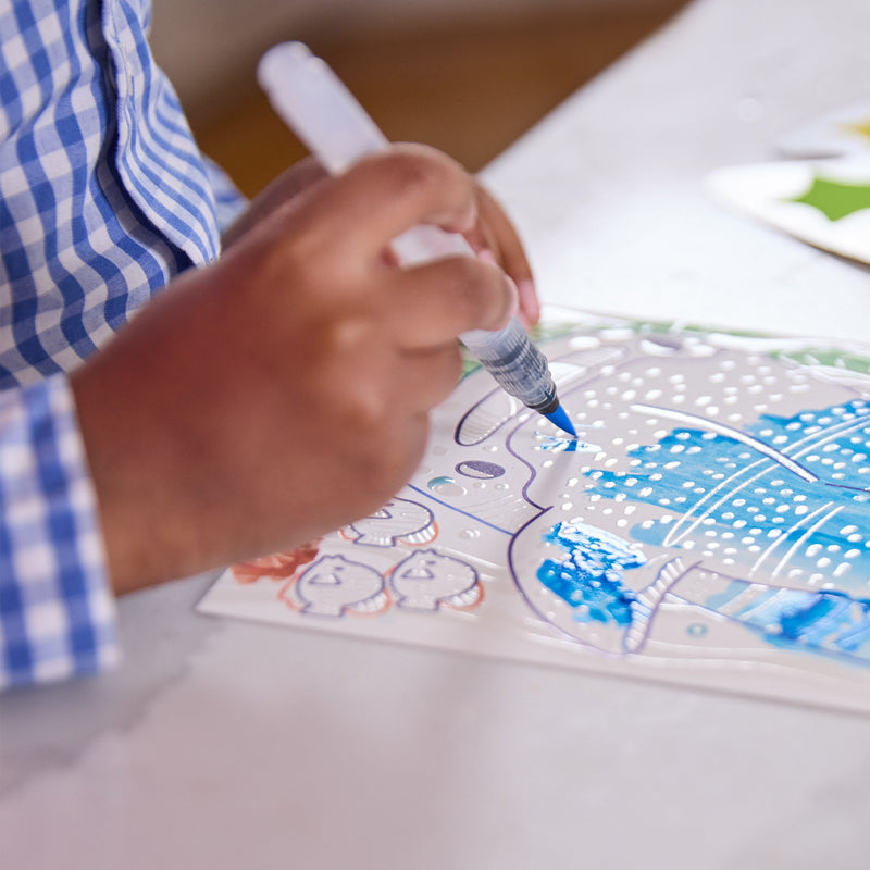 Child coloring ocean-themed watercolor activity book with blue marker pen