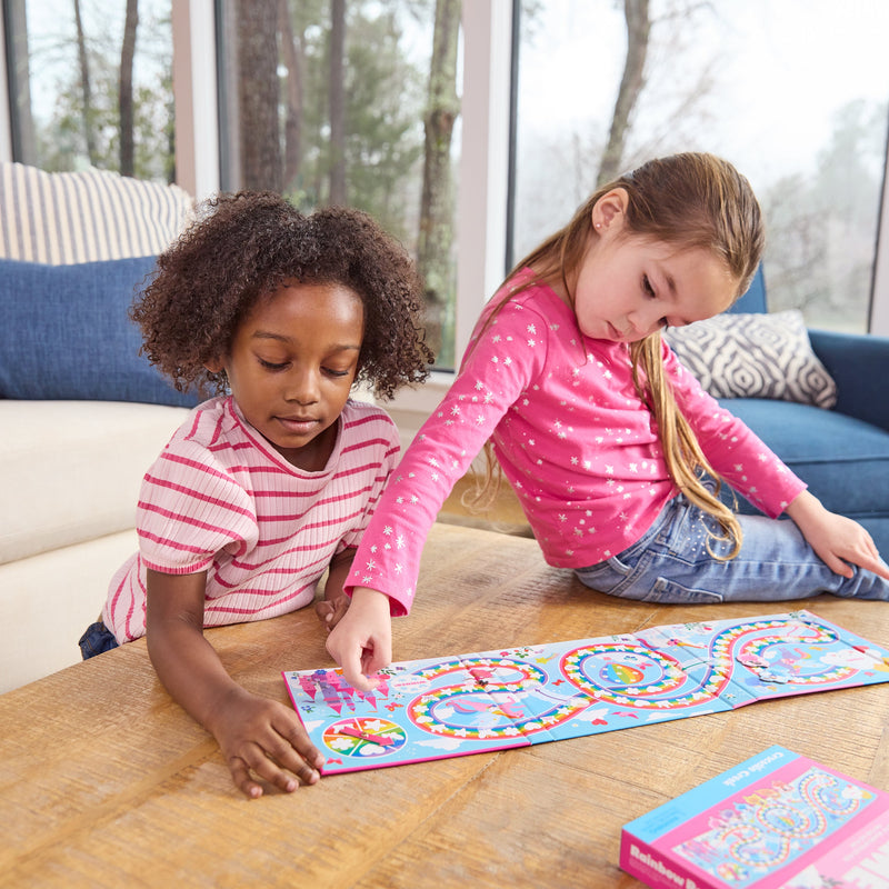 Two children playing Rainbow Race magnetic board game on wooden table.
