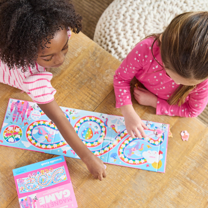Two children playing with Crocodile Creek Magnetic Rainbow Race board game on wooden floor.