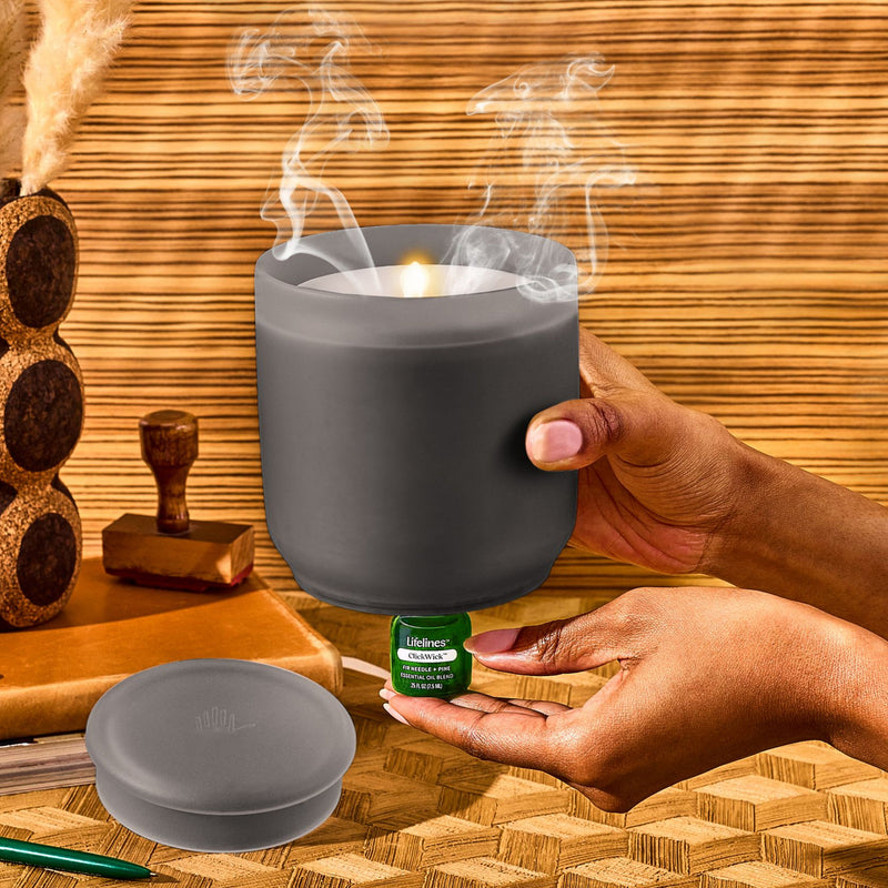 Frosted charcoal flameless candle diffuser with hands holding essential oil bottle in spa setting