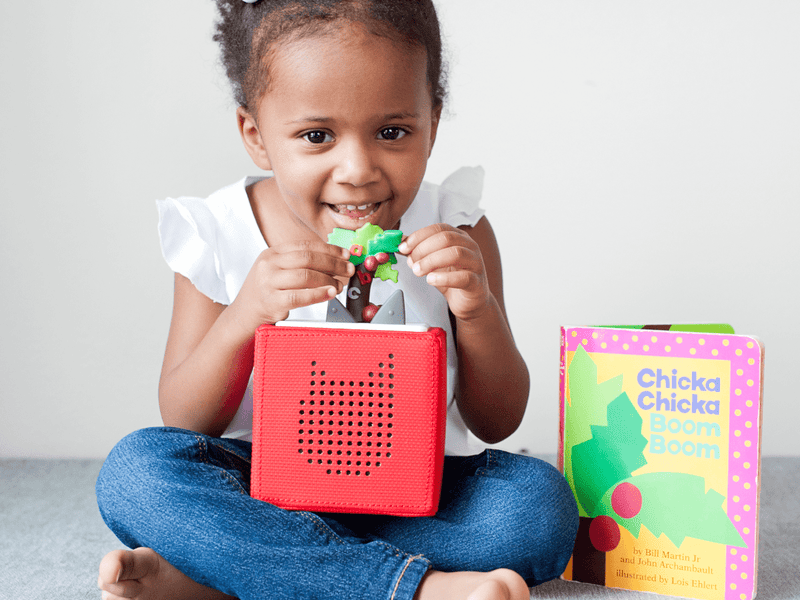 Young girl playing with red Tonie audio player and Chicka Chicka Boom Boom book