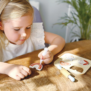 Child playing with a toy cookie baking set on a wooden table.