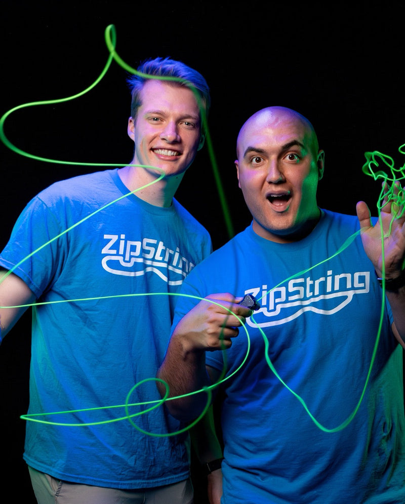 Two people wearing blue ZipString t-shirts demonstrating glowing green ZipString toy in dark setting