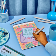 Person using FlowArt dot-by-letter notebook with colorful dotted design saying Joy is Meant to be Shared