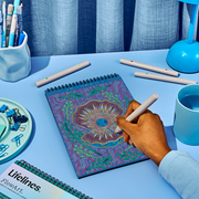 Person creating colorful dot mandala pattern in Lifelines FlowArt notebook with markers