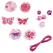 A pink craft kit with various decorative elements including butterfly-shaped and floral resin cabochons, pink cords, small bows, and star-shaped beads on a white background.