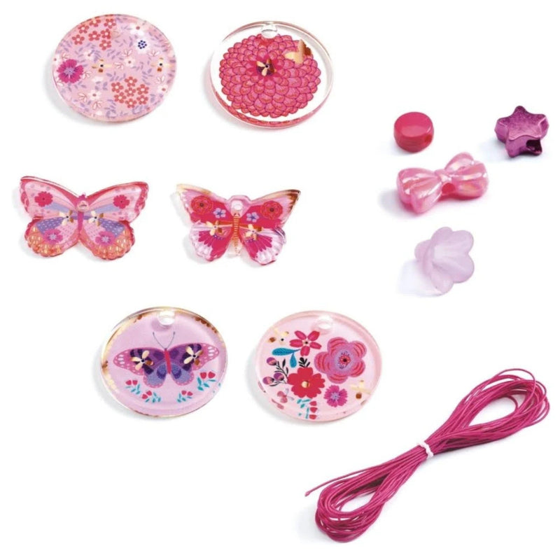 A pink craft kit with various decorative elements including butterfly-shaped and floral resin cabochons, pink cords, small bows, and star-shaped beads on a white background.