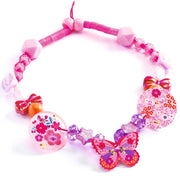 A pink beaded necklace with decorative charms, including a butterfly, floral heart, floral disc, and small bows, on a white background.