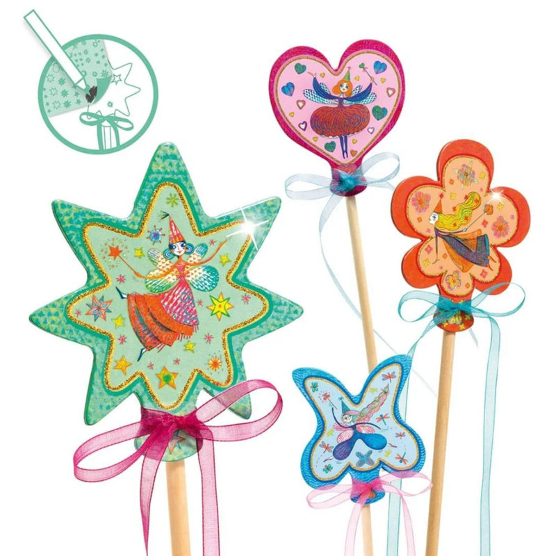 Four colorful wizard-themed wand toppers on wooden sticks, including a star, heart, flower, and butterfly shape, decorated with whimsical illustrations and tied with pink, white, and light blue ribbons. A small circular inset in the top left shows a close-up of one of the toppers.