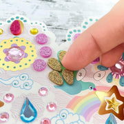 Colorful sticker sheet with decorative elements and a hand placing a gold glittery sticker.