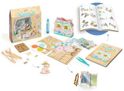 A children's wooden dollhouse craft kit laid out on a white background, showing the assembled/boxed house, wooden sticks, paint palette, instruction booklet, stickers, tweezers, and small decorative pieces. No person, animal, or real environment is present, so this is Product/Packaging rather than Lifestyle.