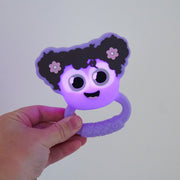 Hand holding purple Glo Pals Lumi Rattle with cute face and dark hair