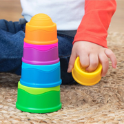 Child playing with Dimpl Stack silicone baby toy from Fat Brain. Colorful stackable cups sitting on tan mat.