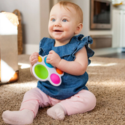 Baby sitting on a carpeted floor holding a Dimpl toy from Fat Brain Toy Co.