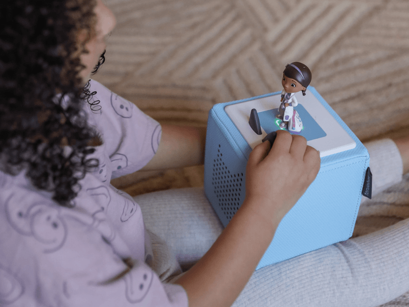 Child's hand using Tonie Disney Doc McStuffins figure on blue Toniebox audio player