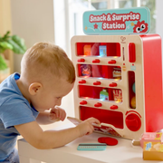 Young toddler exploring Hape Snack and Surprise Station toy vending machine with lights