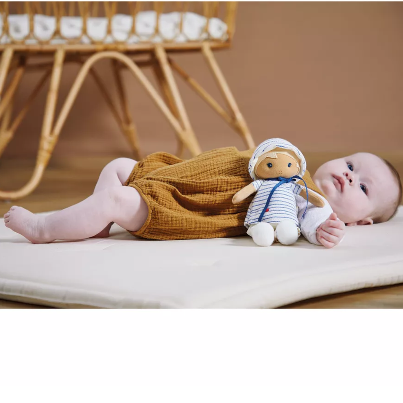 Baby lying on a mat with the Eli doll, with a crib in the background.