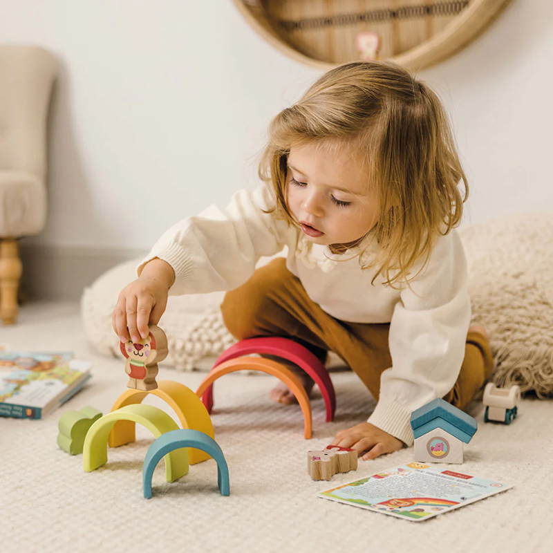 Child playing with set of colorful wooden toys from Bababoo including a rainbow, car, and animal figures on a white background.