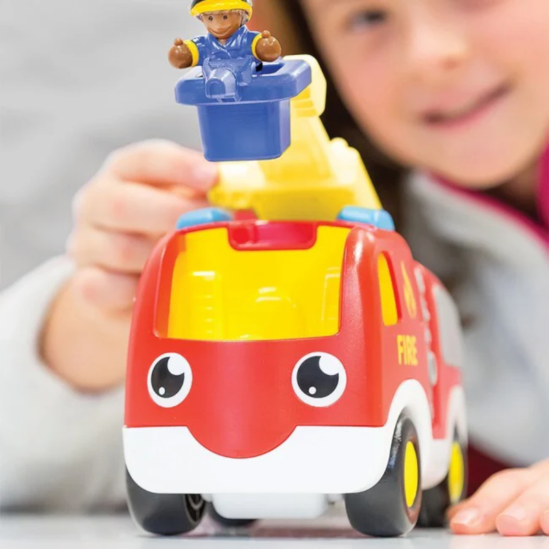 Child holding a toy fire truck with a figurine on top, blurred background.