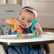 Child playing with teething rings from Fat Brain called pipSquigs Loops. Colorful toys are suction cupped to highchair table.