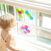 Child playing with colorful flower-shaped Whirly Squigs from Fat Brain on a window.