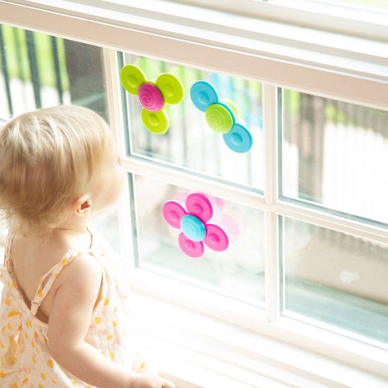 Child playing with colorful flower-shaped Whirly Squigs from Fat Brain on a window.