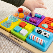 Colorful toy with various textured blocks and a child's hand interacting with it, featuring Fat Brain Toy Co. branding.