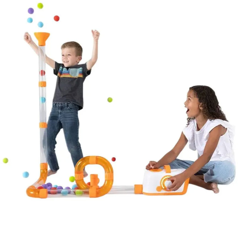 A child stands near a clear plastic track launching colorful balls into an orange funnel, while another child sits beside a white ball dispenser with an orange loop on a white background.