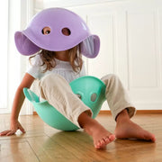 Child playing with purple and turqoise Billibos resembling a creature on a wooden floor.