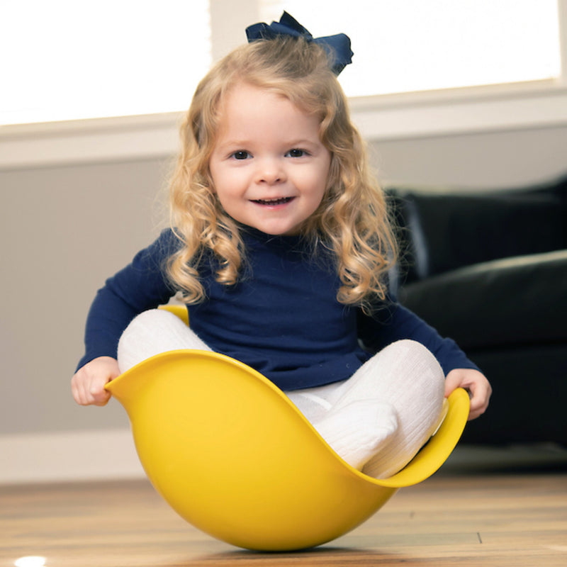 Child sitting on a yellow Bilibo indoors.