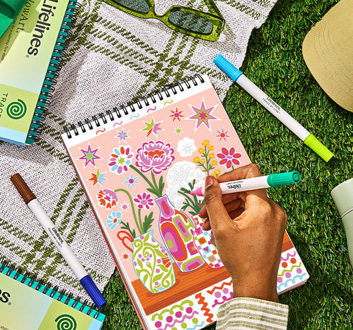 Hand coloring floral artwork with colorful scented markers on grass with notebooks