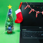 Decorate Your Christmas Desk kit contents including a small lighted tree, stocking, candy cane garland & strig of lights against the screen of a black laptop.