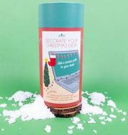 Decorate Your Christmas Desk kit in cylindrical tube on green background with artificial snow.