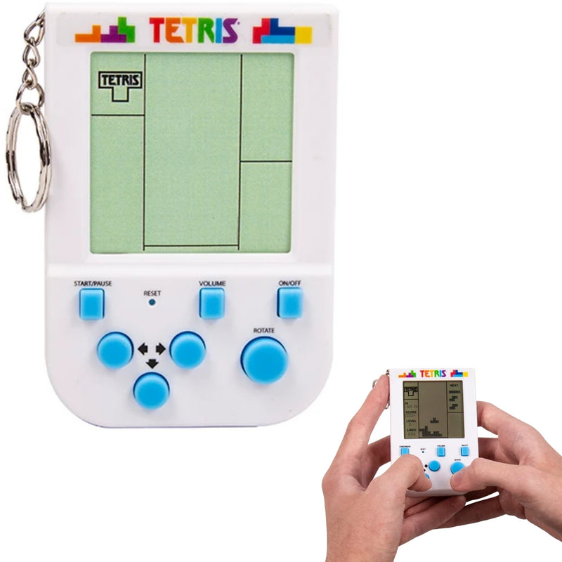A white Tetris handheld game console with a green LCD screen, blue buttons, and a keychain ring, shown alongside a person's hands holding a smaller version of the device.