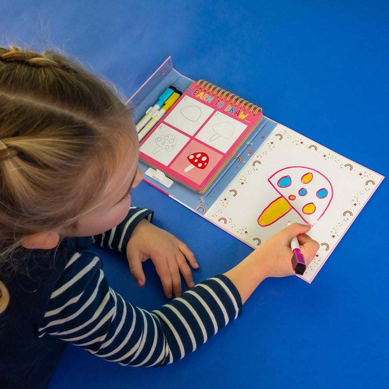 Child coloring a picture of a pizza in a coloring book on a blue table.