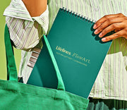 Person holding green Lifelines FlowArt dot-by-letter notebook in green tote bag