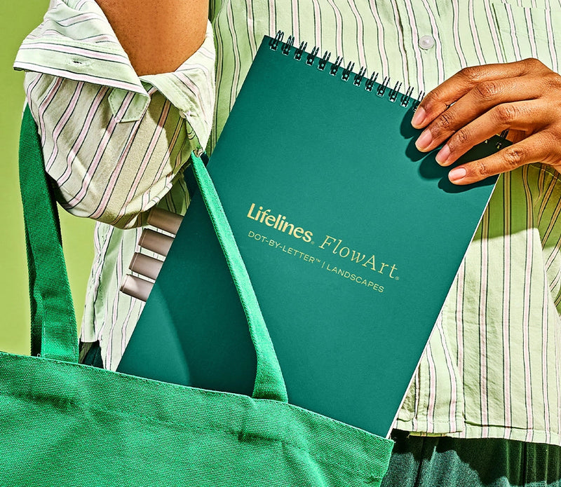 Person holding green Lifelines FlowArt dot-by-letter notebook in green tote bag
