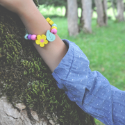 Brightly colored, wooden bead flower bracelet on wrist leaning against tree.  