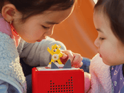 Children playing with yellow Care Bears Funshine Bear Tonie on red Toniebox speaker