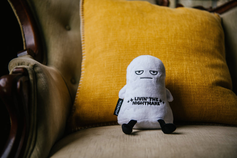 White ghost plushie with 'Livin' the Nightmare' text sitting on yellow chair