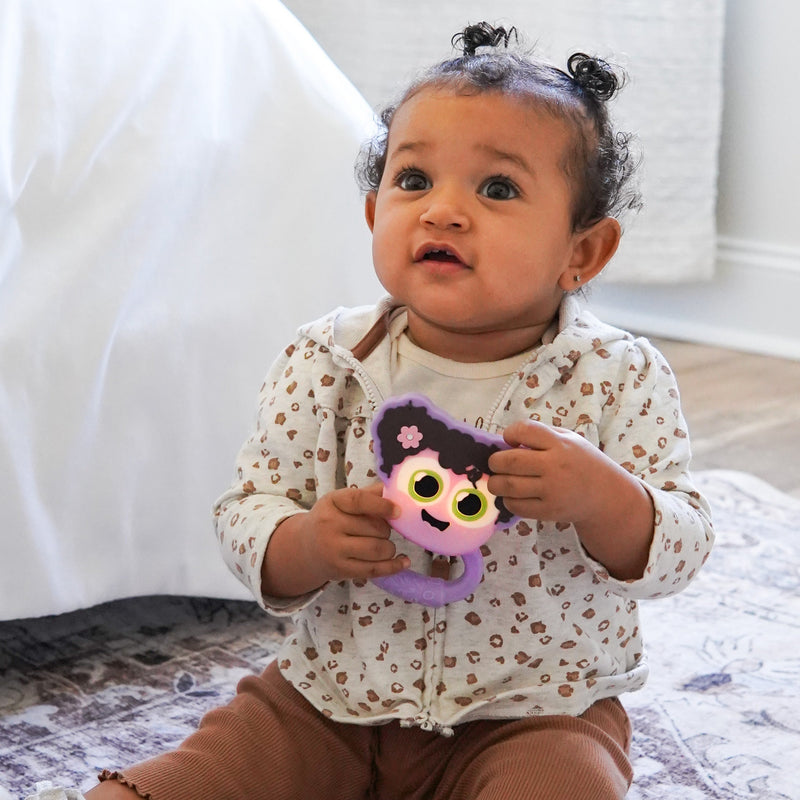 Baby holding purple Glo Pals Lumi Rattle with character face and flower detail