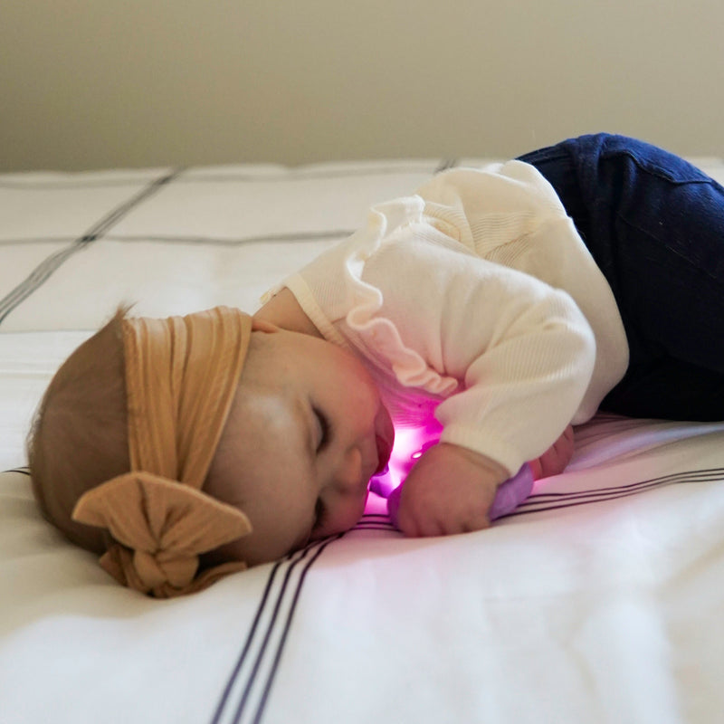 Baby lying down holding glowing pink Glo Pals Lumi Rattle with light activated