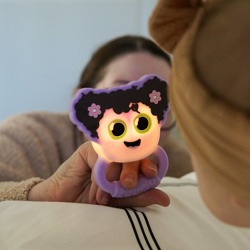 Child holding illuminated Glo Pals Lumi Rattle with cute character face and purple silicone ring